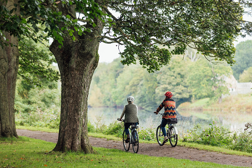 Rear view shot of an LGBTQI+ lesbian couples a bike ride together in a public park in Hexham, North East England. They are cycling side by side along a rivers edge.