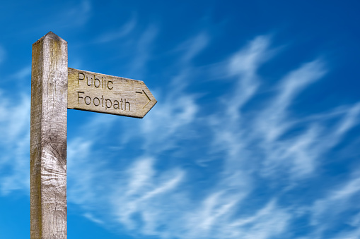 A weathered wooden public footpath sign against a blue sky pointing the way with copy space.