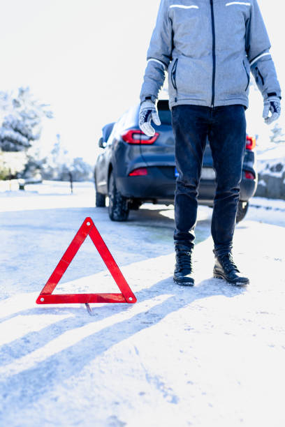 istock Broken car concept. Man with warning triangle on road covered with snow. 2010344943