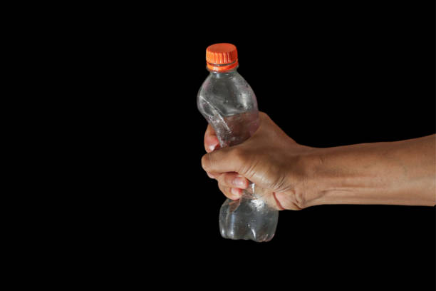 Person's Hand Squeezing Plastic Empty Mineral Water Bottle on Isolated Black Background. Plastic pollution concept.