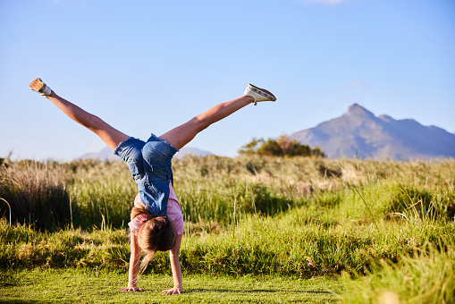 Rear view of a carefree little girl doing cartwheels outside in a field in a nature reserve in summer
