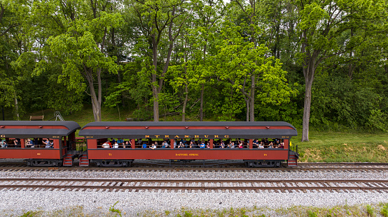 Strasburg, Pennsylvania, May 20, 2023 - A Drone Side View of an Antique Open Air Passenger Coach, With Passengers Waving, on a Sunny Day