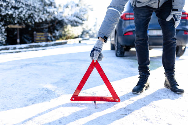 istock Broken car concept. Man placing warning triangle on road covered with snow. 2010357496