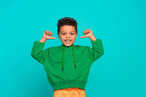 Photo of cheerful charming boy dressed stylish green clothes thumbs pointing himself isolated on cyan color background.