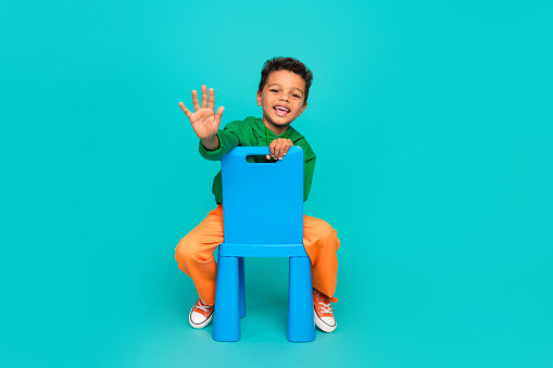 Photo of cute charming boy wear stylish green clothes sitting chair in playroom have fun empty space isolated on cyan color background.