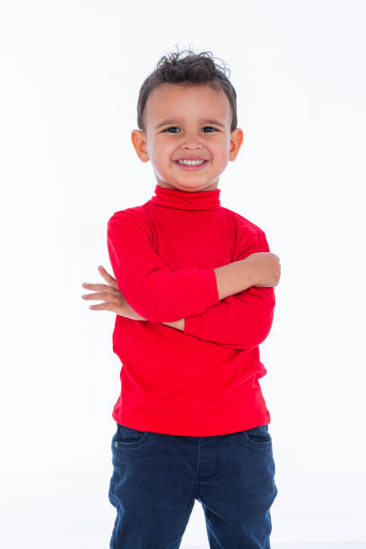 Latin boy with dark skin and curly hair is inside a photography studio where he models a children's clothing line while enjoying the moment and looking at the camera.