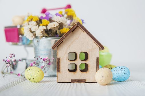 Happy Easter greeting card. Miniature wooden house. Rabbits, colorful eggs, spring flowers with tag for text.