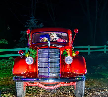 Vintage Red Mack Truck Decorated With Christmas Lights And Wreaths, Featuring Stuffed Animal Passengers In The Front Seat, Parked At Night.