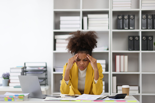 Stress and pressure of overwork. African woman in office stressed with paperwork and worried about not meeting deadlines.