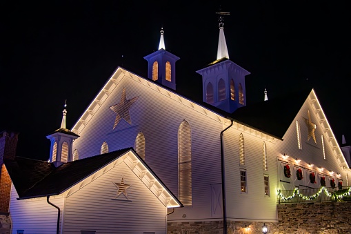 Illuminated White Church Adorned With Christmas Wreaths And Stars At Night, Showcasing Its Architectural Detail And Warm Glow Against The Dark Sky.
