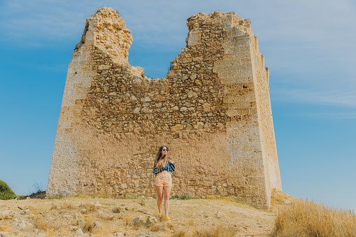Female with long hair in shorts and sunglasses walking at the scenic landscape exploring old built structures in Gallipoli, South Italy