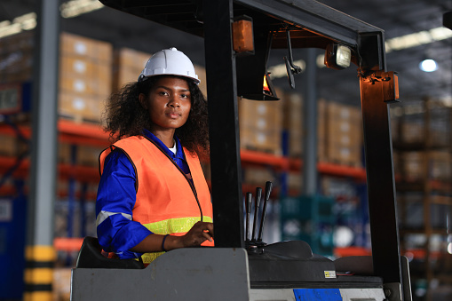 Confident young black female worker driving a forklift around the floor of a distribution warehouse