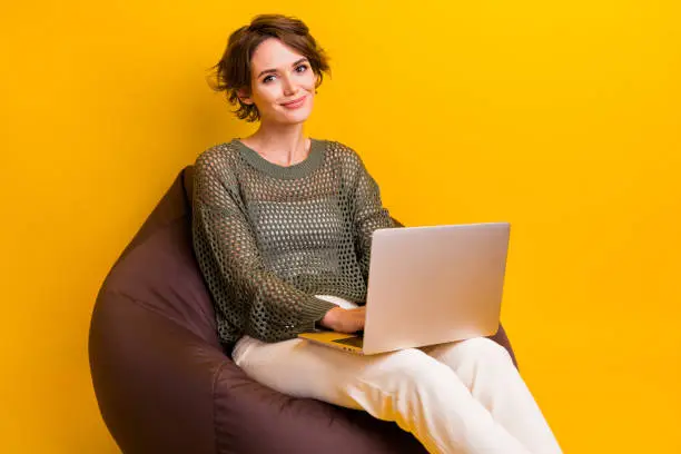 Photo of Photo of cute lovely girl wear stylish clothes sitting bean bag modern macbook netbook empty spcace isolated on yellow color background