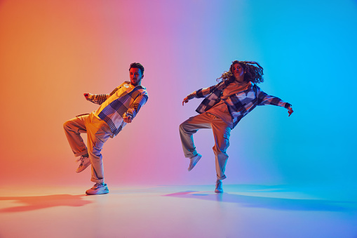 Dynamic photo of two dancers, man and woman move synchronously in hip-hop style dance against gradient background in neon light. Concept of movement, energy, dance battles. Dynamic gel portrait