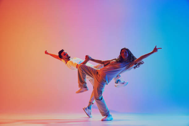 istock Two talented dancers mid-movement performing in vibrant pink and blue lighting against gradient background. Dynamic poses, contemporary attire. 2010497882