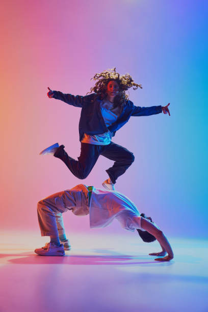 istock Acrobatic dance pair, woman jumping and man in handstand, against gradient studio background in neon light, filter. 2010497921