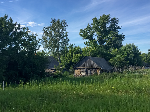 Side view of old weathered abandoned wooden house on green grass in countryside in a sunny summer day. Soft focus. Rural depopulation theme.