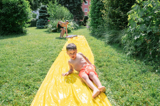 Brothers playing sliding trough a slippery plastic in the garden yard in summer