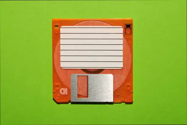 Top view of blank paper with lines stuck on brown floppy disk on green background