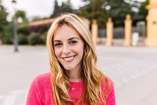 Happy young beautiful woman smiling at camera standing at street. Portrait of millennial girl with toothy smile feeling positive over urban city background.