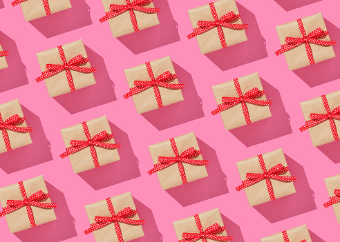 Pattern of brown gift boxes on with red bows on pink background