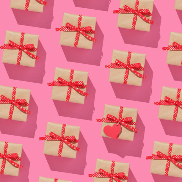 istock Pattern of brown gift boxes on with red bows on pink background. One present with heard-shaped tag. 2010659169