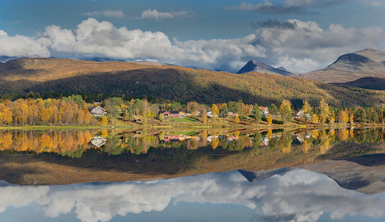 beautiful scenic landscape with mountain and autumnal forest under the sky reflecting in surface of water in Norway.