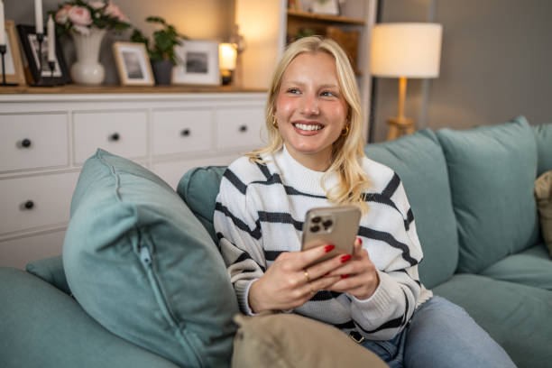 istock Young attractive charming smiling woman in casual home clothes lying on sofa and using mobile phone to text 2010666080