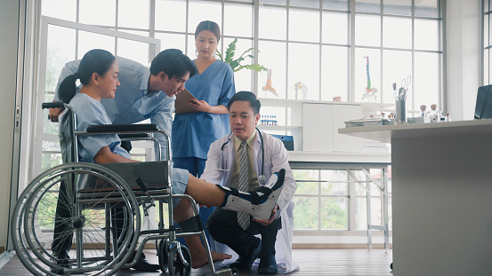 A patient with a leg injury in a wheelchair came to see the doctor at the hospital with his son accompanying him.