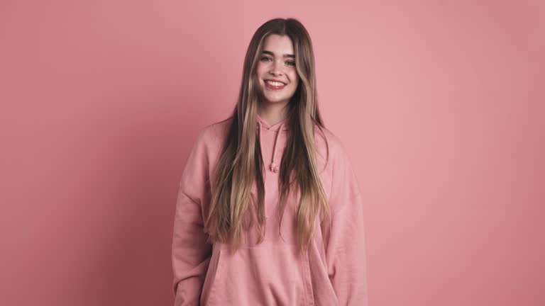 Positing woman with long hair smiling in pink studio