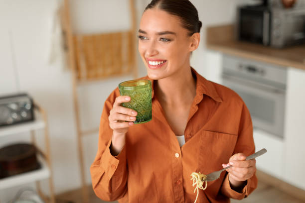 istock Smiling woman with a drink and spaghetti in modern kitchen 2010703409
