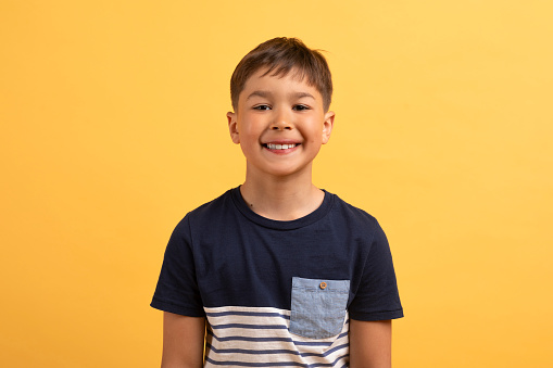 Cheerful happy handsome cute kid school boy wearing casual outfit posing isolated on yellow background, smiling at camera, showing his teeth. Childhood, kids concept