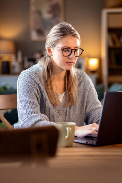 istock Smiling young woman working at home using laptop while sitting in her living room. 2010760661