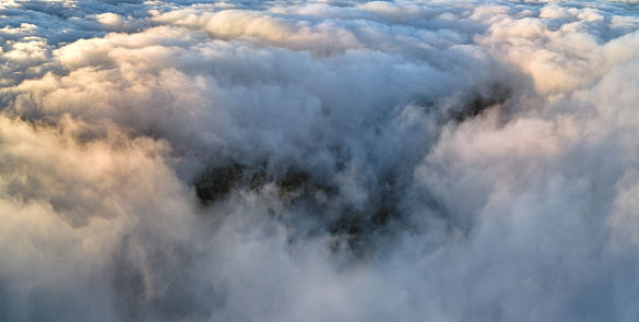 Aerial view from airplane window at high altitude of dense puffy cumulus clouds flying in evening.