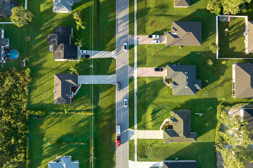 Aerial view of street traffic with driving cars in small town. American suburban landscape with private homes between green palm trees in Florida quiet residential area.