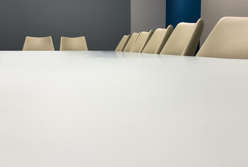 Eight cream desk chairs along the edge of a clean white conference table in a modern office space.