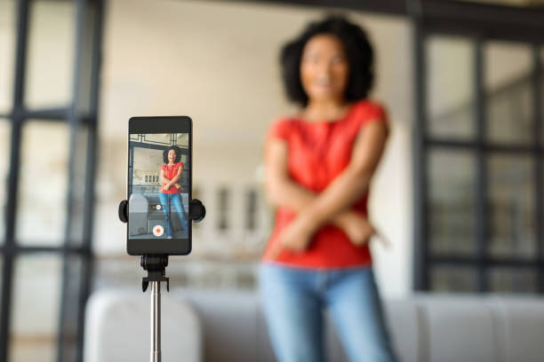 istock Smiling black woman vlogging, using smartphone on tripod at home 2010782172