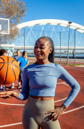 Portrait of young African American woman with her female friends on basketball court holding ball in her hands.