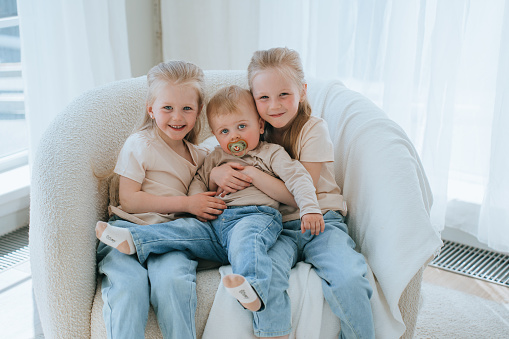 Three siblings cuddling on a chair, cozy home setting
