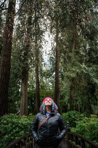 A young woman in a jacket, looking up to the lush trees in the forest of Cannon Beach, Oregon.