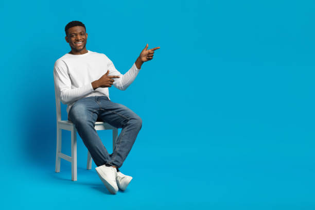 istock Relaxed african guy sitting on chair, pointing at copy space 2010805899