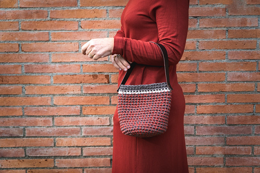 body of a woman in profile leaning on a brick wall, wearing casual clothing and a handbag hanging from her arm. Shoot without head