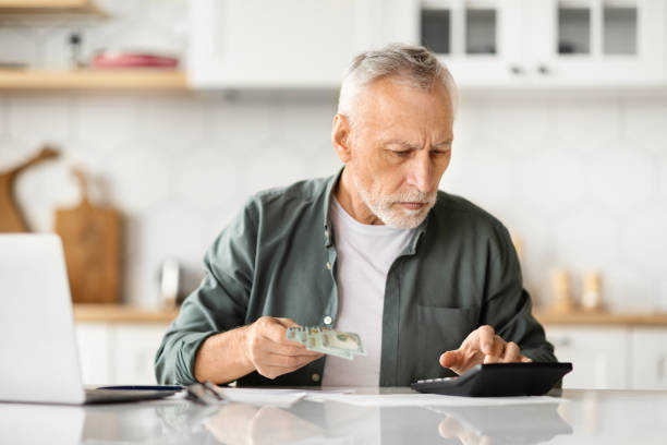 istock Focused elderly man holding money cash and using calculator at home 2010826888