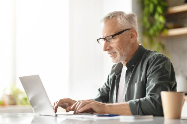 istock Happy elderly gentleman typing on laptop, enjoying his work in sunny kitchen 2010826987