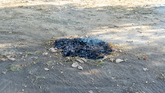 Piles of burned garbage, soot and smoke rising into the air. It's like the fire just went out. The remains of dried leaves were burned and turned black. The surrounding area is a mixture of loose,