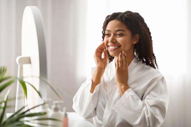 istock Smiling black woman at home touching face while looking in mirror 2010865670
