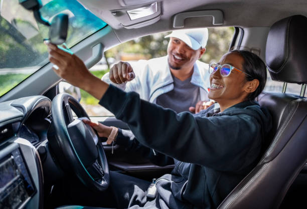 istock Smiling female student adjusting car rear-view mirror during driving lesson 2010866214