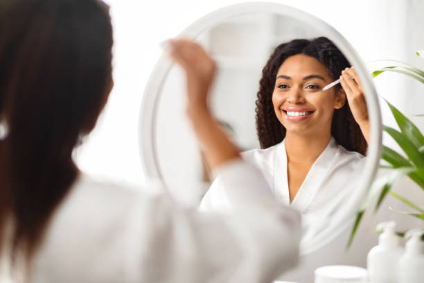 istock Beautiful Black Female Applying Moisturising Serum On Face While Standing Near Mirror 2010866221