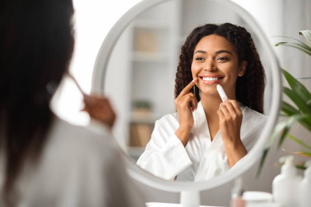 istock Beautiful Black Lady Looking At Mirror And Applying Moisturising Lip Balm 2010866771