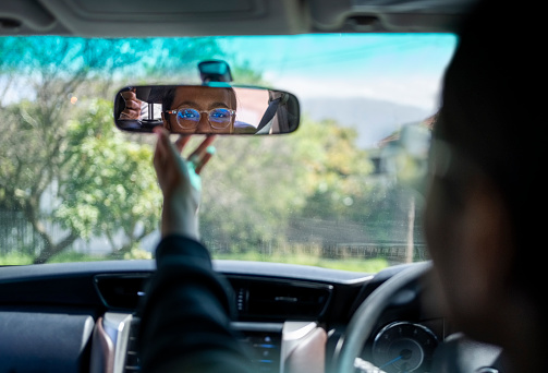 Rear view of a teenage girl adjusting the rear view mirror in the car during her driving practice